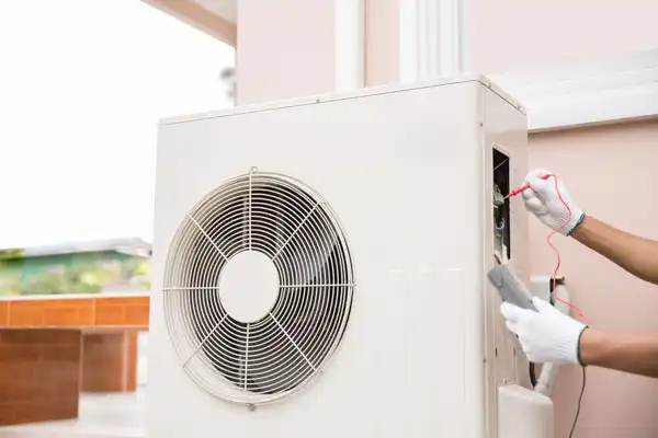 A Coast to Coast technician in white gloves inspects an outdoor AC unit, ensuring quality service at a customer's building exterior.
