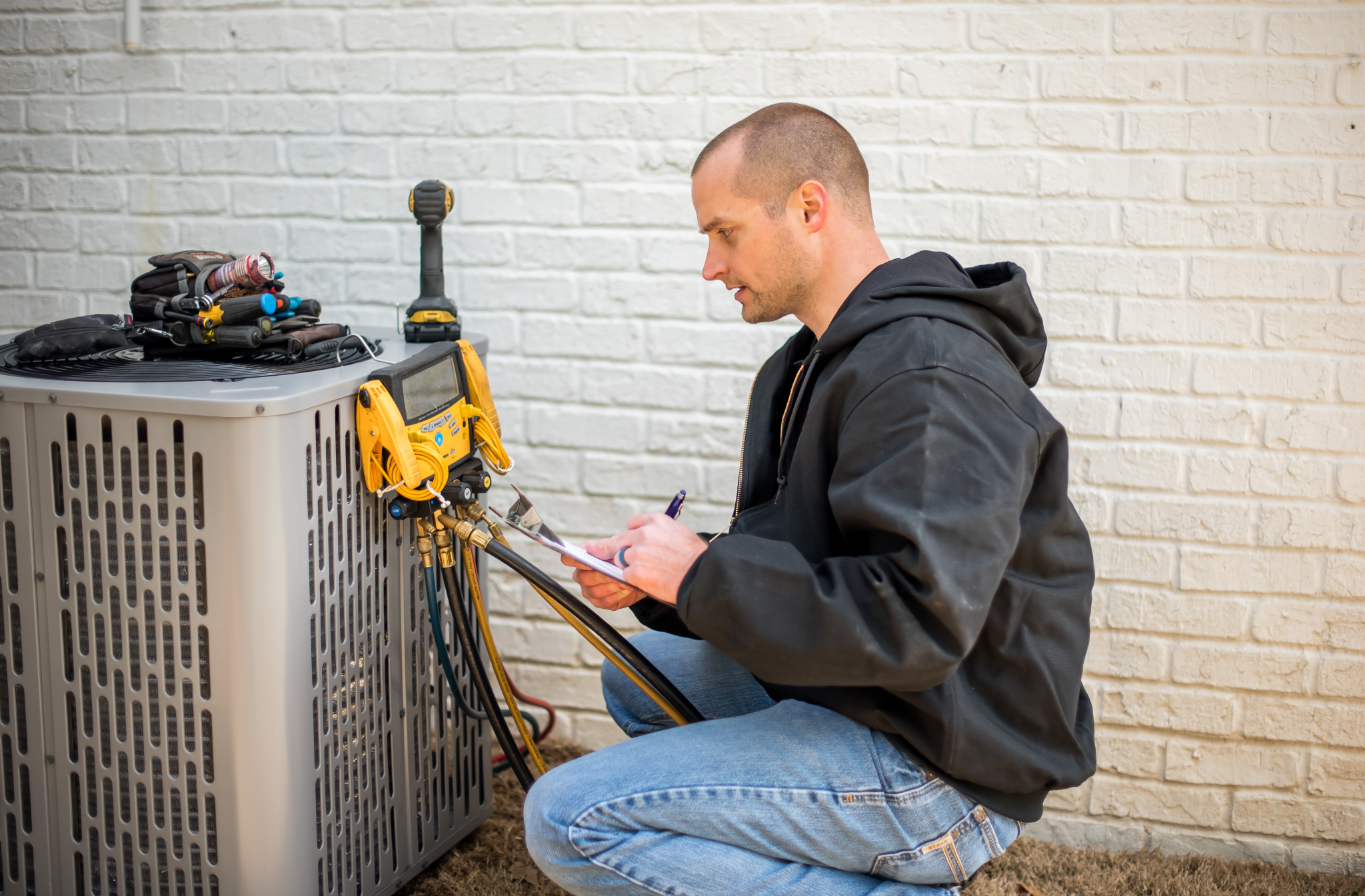 A Coast to Coast technician in a black jacket checks an outdoor HVAC unit, using diagnostic tools and recording notes on a clipboard.