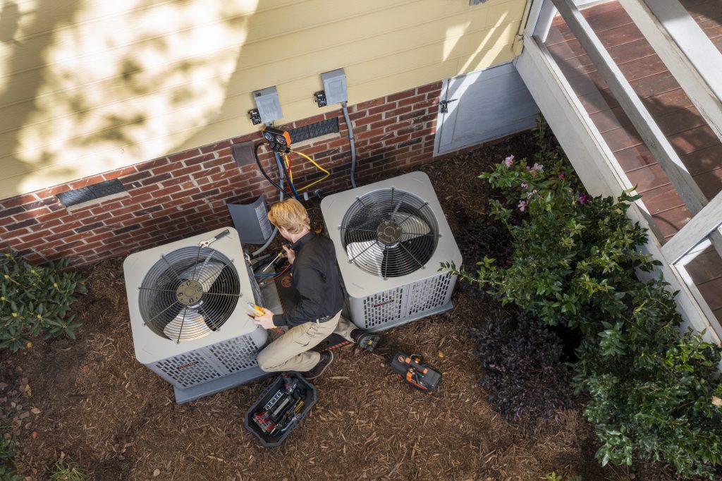 A Coast to Coast technician services two outdoor AC units beside a home, expertly using tools and diagnostic equipment.