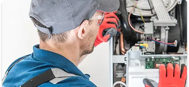A Coast to Coast technician in protective gear carefully inspects and repairs the inside of a boiler or HVAC unit on-site.