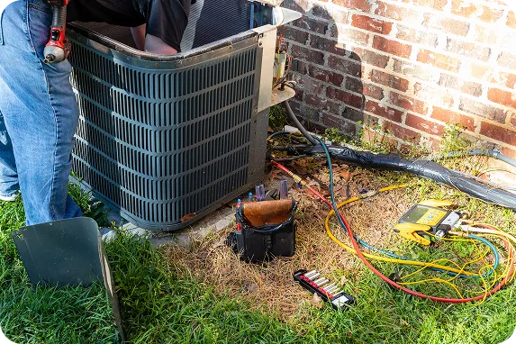 A Coast to Coast technician services an outdoor AC unit, with tools and equipment arranged on grass by a brick wall.