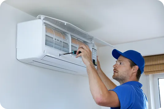 A Coast to Coast technician in a blue uniform skillfully services a wall-mounted AC unit with a screwdriver for our valued customers.